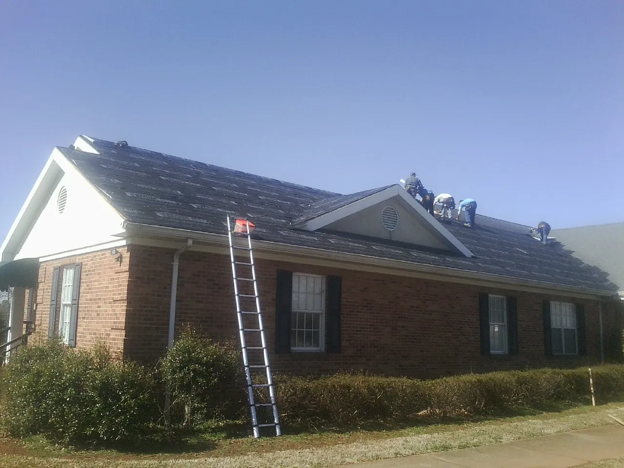 Crew tearing shingles off a brick ranch roof with a ladder set — Metal Roof Repair work by our crew in Marathon